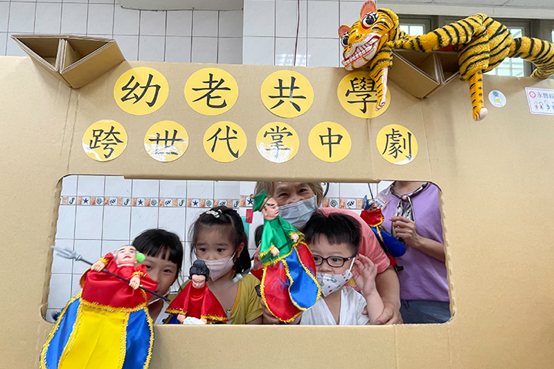長輩與孩童一同在戲臺後方開心地展示布袋戲偶